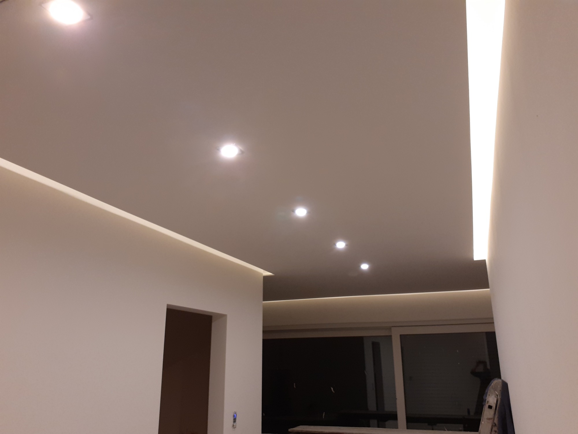 Sufit podwieszany z oświetleniem punktowym i listwami LED, widok z dołu na białą powierzchnię z równomiernie rozmieszczonymi okrągłymi lampami i liniowymi źródłami światła wzdłuż krawędzi.