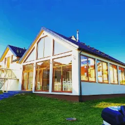 Nowoczesny, parterowy budynek z dużymi przeszkleniami i drewnianą stolarką okienną, otoczony zielonym trawnikiem i błękitnym niebem.