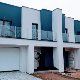 Nowoczesny budynek bliźniaczy z balkonami zabezpieczonymi szklanymi balustradami na pierwszym piętrze, widok z zewnątrz w trakcie prac wykończeniowych.