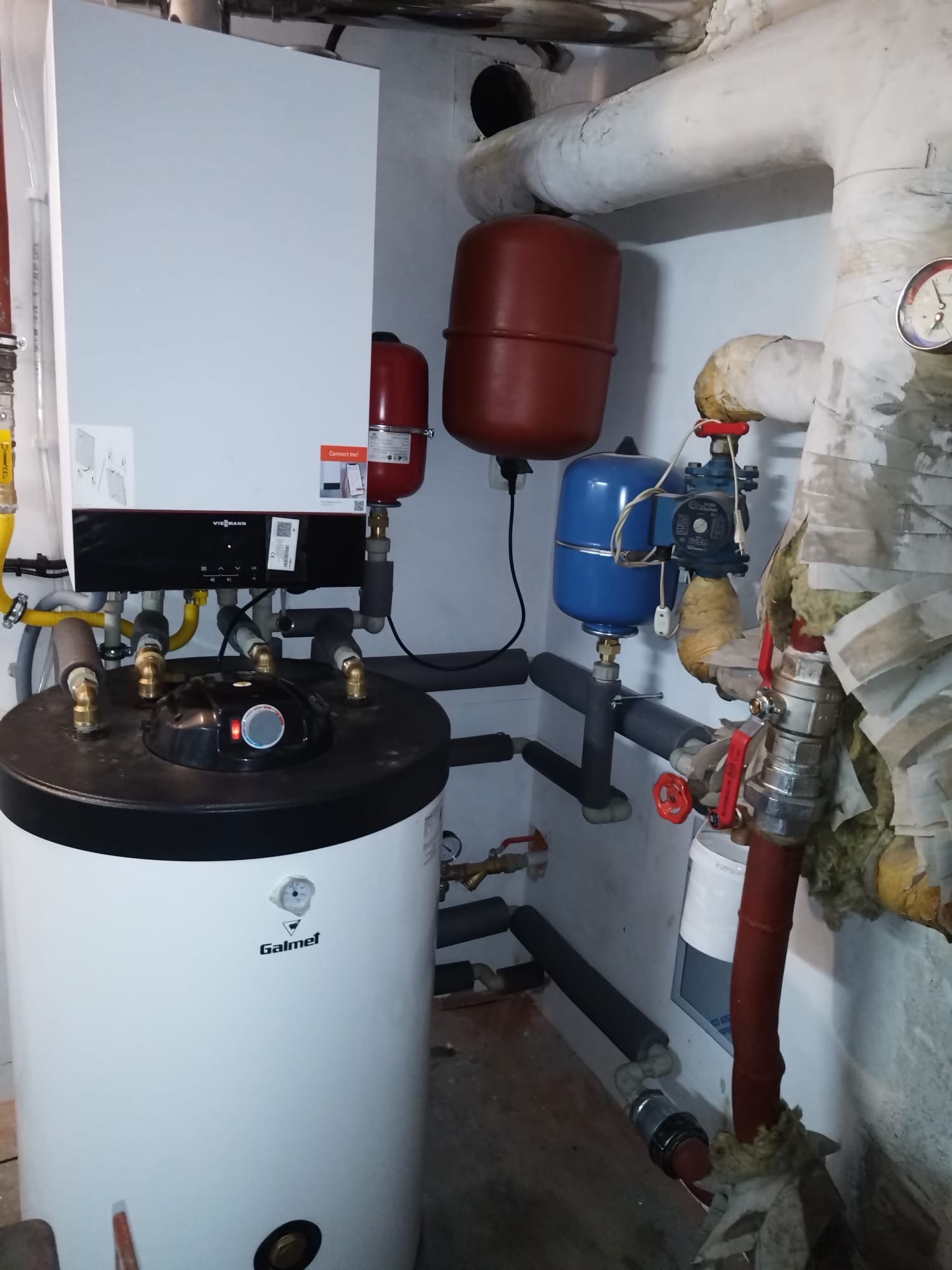 Nowoczesny piec gazowy Viessmann z zasobnikiem Galmet w kotłowni. Widoczne rury, zawory, zbiorniki wyrównawcze. Oświetlenie sufitowe.