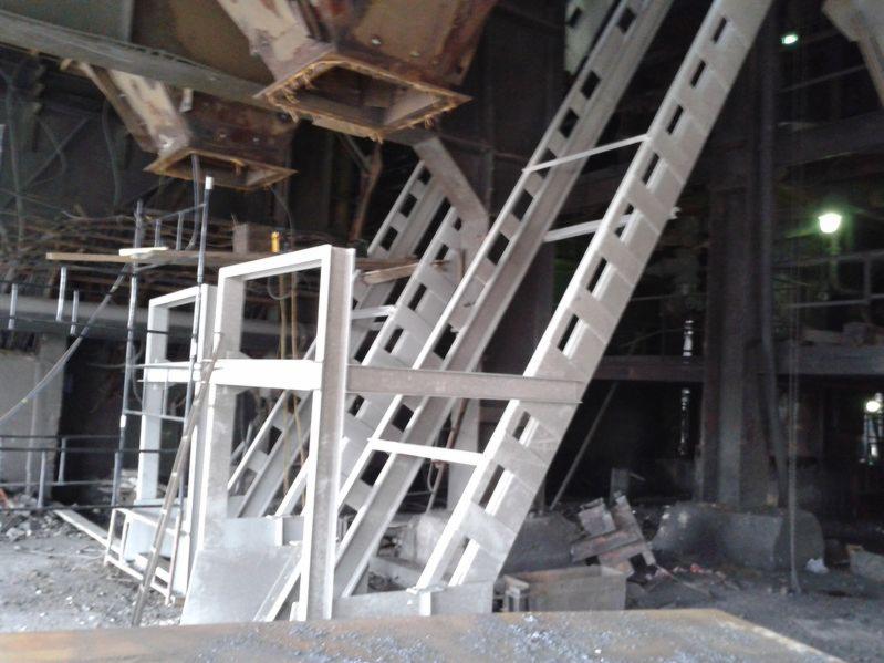 Konstrukcja stalowa w hali przemysłowej w trakcie montażu, widoczne elementy nośne i rusztowania, surowe oświetlenie.