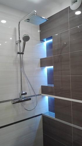 Nowoczesna kabina prysznicowa z deszczownicą i półkami z podświetleniem LED w wykończonej łazience, płytki w odcieniach szarości i bieli z dekoracyjnym paskiem.