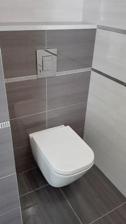 Nowoczesna toaleta podwieszana w łazience wykończonej szarymi i białymi płytkami z dekoracyjnymi paskami.