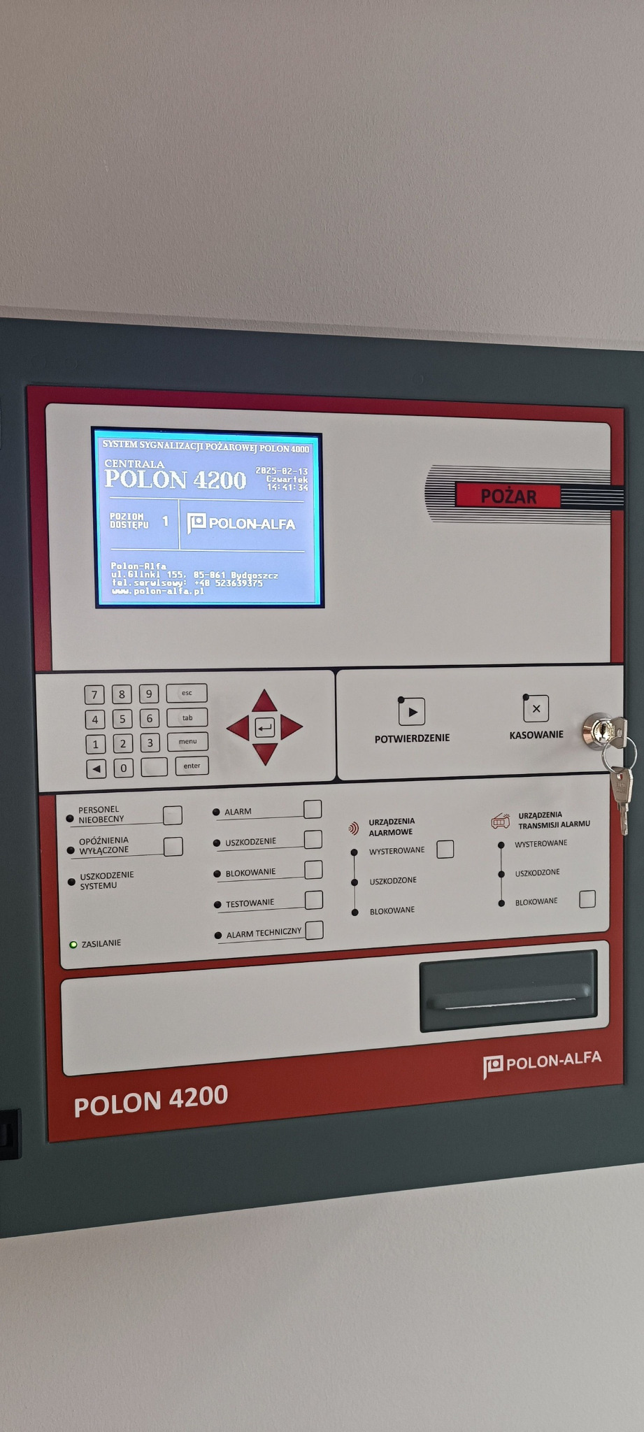 Centrala systemu sygnalizacji pożarowej Polon 4200 z wyświetlaczem, klawiaturą i przyciskiem 'Pożar'. Widoczne diody statusu i kluczyk w zamku.
