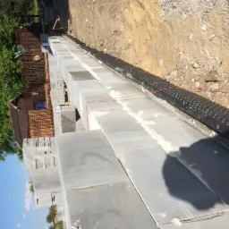 Wznoszenie muru fundamentowego z bloczków betonowych, widoczna izolacja pionowa fundamentów oraz czerwona linka wyznaczająca poziom, w tle drewniana altana.