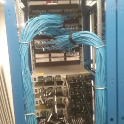 Szafa rack z serwerami i przełącznikami, uporządkowane niebieskie kable sieciowe spięte opaskami, czarne kable zasilające, widoczne wentylatory i diody LED.