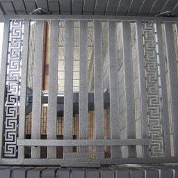 PawelSpawTech - Szara metalowa furtka z pionowymi prętami i dekoracyjnym wzorem meandrycznym po bokach, widok od strony zamka.