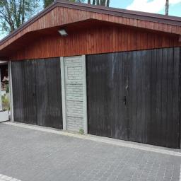 PawelSpawTech - Dwuskrzydłowa, ciemna brama garażowa w budynku z drewnianą elewacją i betonowymi elementami, widok z zewnątrz na kostkę brukową.