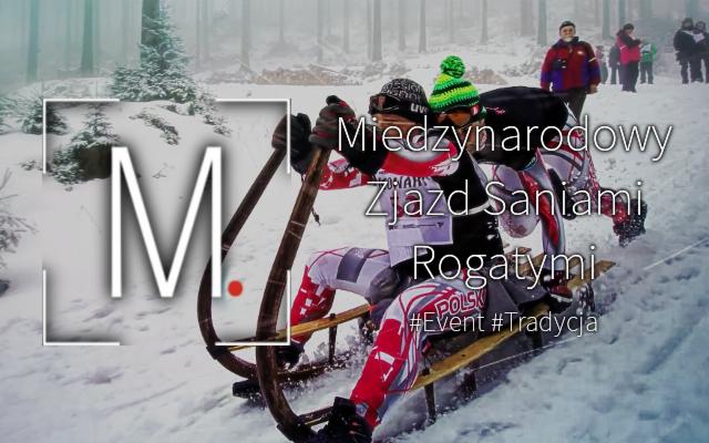 Dwóch zawodników w kaskach i kombinezonach zjeżdża na drewnianych saniach po ośnieżonym stoku podczas 'Międzynarodowego Zjazdu Saniami Rogatymi', w tle widoczni kibice i drzewa.