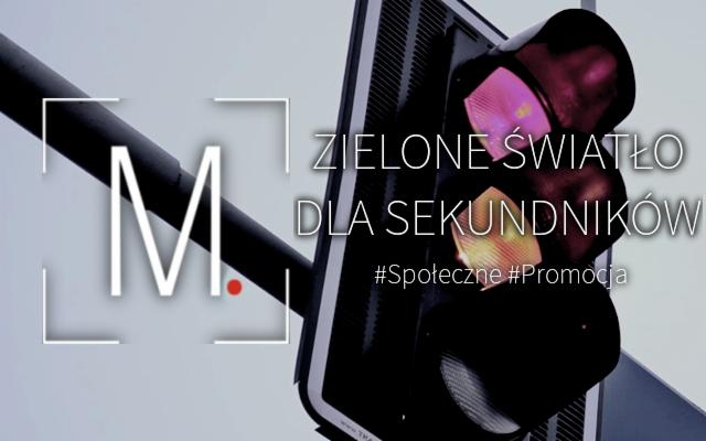 Sygnalizacja świetlna z napisem 'Zielone światło dla sekundników' i hasztagami #Społeczne #Promocja, obok widoczny element logo z literą M.