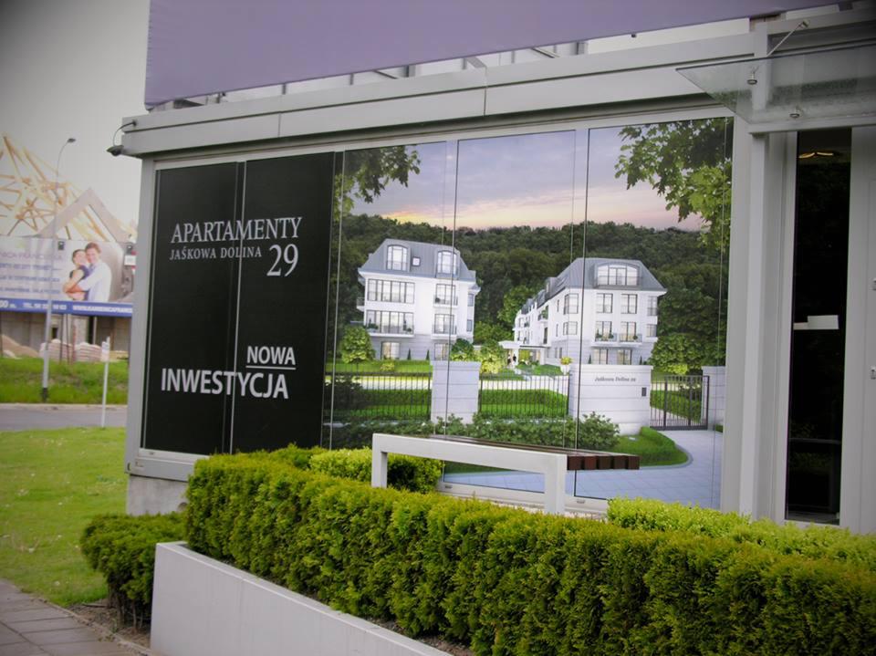 Wizualizacja nowej inwestycji apartamentów Jaśkowa Dolina 29 na plakacie w przeszklonej wiacie przystankowej, z widocznymi budynkami i otoczeniem.