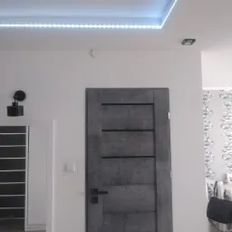 Wnętrze mieszkania z dwoma parami drzwi wewnętrznych o różnym designie, oświetleniem LED podsufitowym i dekoracyjną tapetą w tle.