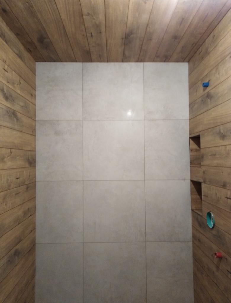 Wykończona łazienka z szarą ścianą wyłożoną dużymi płytkami i drewnianą boazerią na suficie i ścianach bocznych, z wnękami w ścianie bocznej.