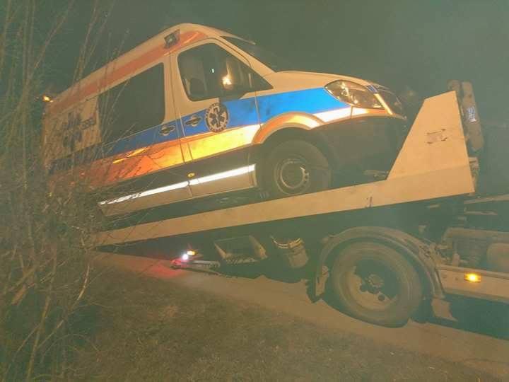 Uszkodzona karetka pogotowia załadowana na lawetę w słabym oświetleniu nocnym.