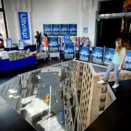 Iluzja optyczna na posadzce: Ulica miejska z budynkami, tworząca wrażenie głębi, na której stoi kobieta.