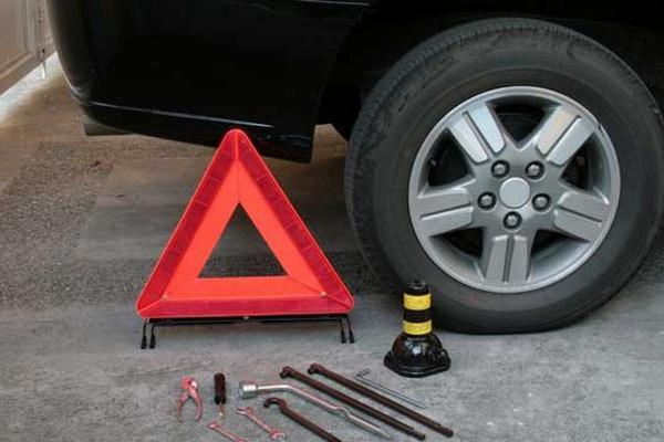 Koło samochodu, trójkąt ostrzegawczy i zestaw narzędzi, w tym podnośnik, na tle betonowej nawierzchni w Myślenicach.