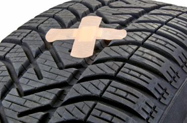 Opona samochodowa z naklejonym plastrem w kształcie krzyża, symbolizująca naprawę lub tymczasowe załatanie uszkodzenia.