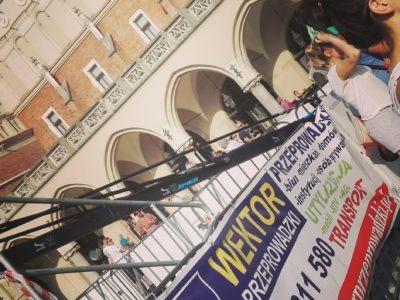 Baner reklamowy firmy przeprowadzkowej Wektor na tle Rynku Głównego w Krakowie, widok z boku, lekko pochylony.