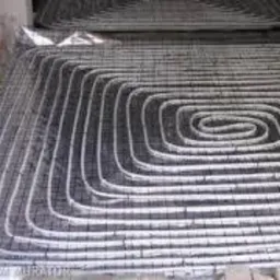 Równomiernie rozłożone rury systemu ogrzewania podłogowego, zamocowane do siatki zbrojeniowej, przygotowane do zalania wylewką betonową.