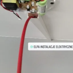 Wnętrze czujnika dymu/tlenku węgla zamontowanego na suficie, z widocznymi bateriami i elektroniką, z wystającym czerwonym przewodem.