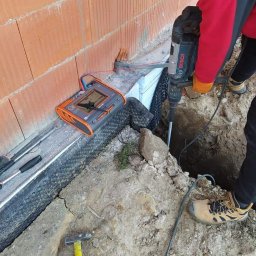 ELPA Instalacje Elektryczne - Pomiar rezystancji uziomu przy budynku z cegły, z użyciem miernika i wiertarki udarowej Bosch, widoczne narzędzia i wykop.