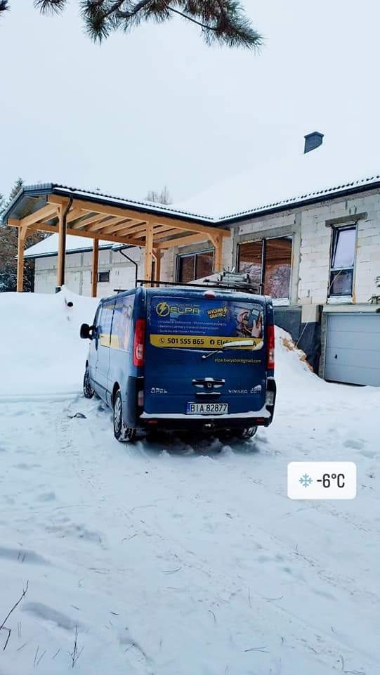 Niebieski van Opel Vivaro z logo firmy elektrycznej ELPA zaparkowany na śniegu przed domem w trakcie budowy, widoczna temperatura -6 stopni Celsjusza.