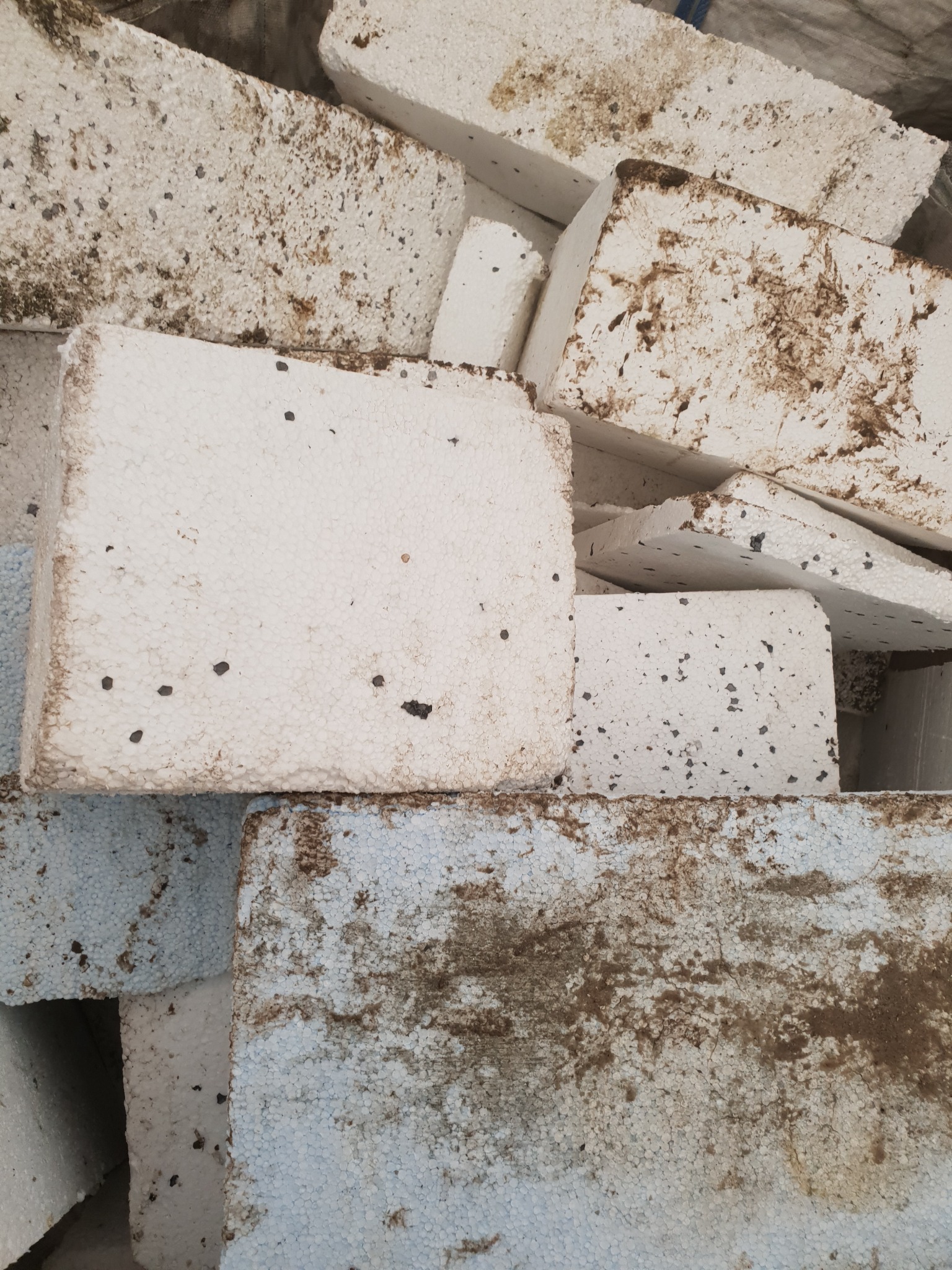 Brudne, białe bloki materiału izolacyjnego z widocznymi śladami ziemi i zabrudzeń, ułożone jeden na drugim.