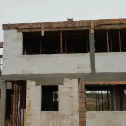 Surowy stan budynku z betonu komórkowego w trakcie budowy. Widoczne drewniane szalunki okienne i zbrojenia. Stan surowy otwarty budynku.