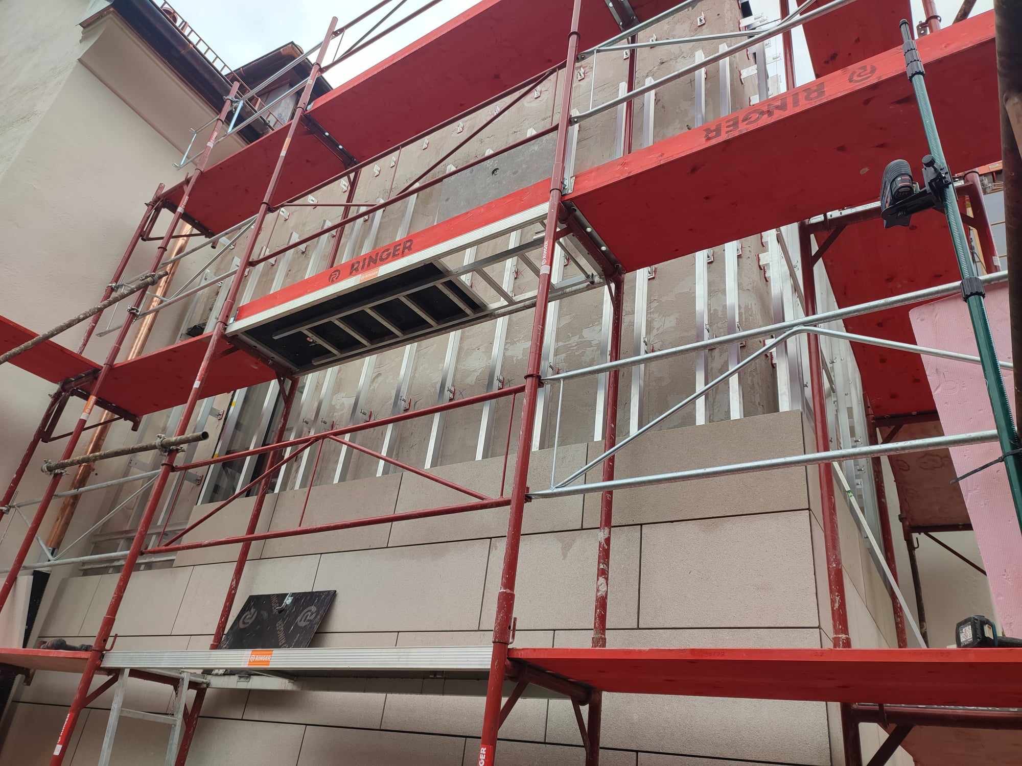 Montaż elewacji z kamiennych płyt na budynku, widoczne rusztowanie Ringer i elementy mocujące.