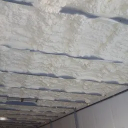 Wnętrze metalowej konstrukcji z natryśniętą, białą izolacją termiczną na suficie, widoczne elementy konstrukcyjne.