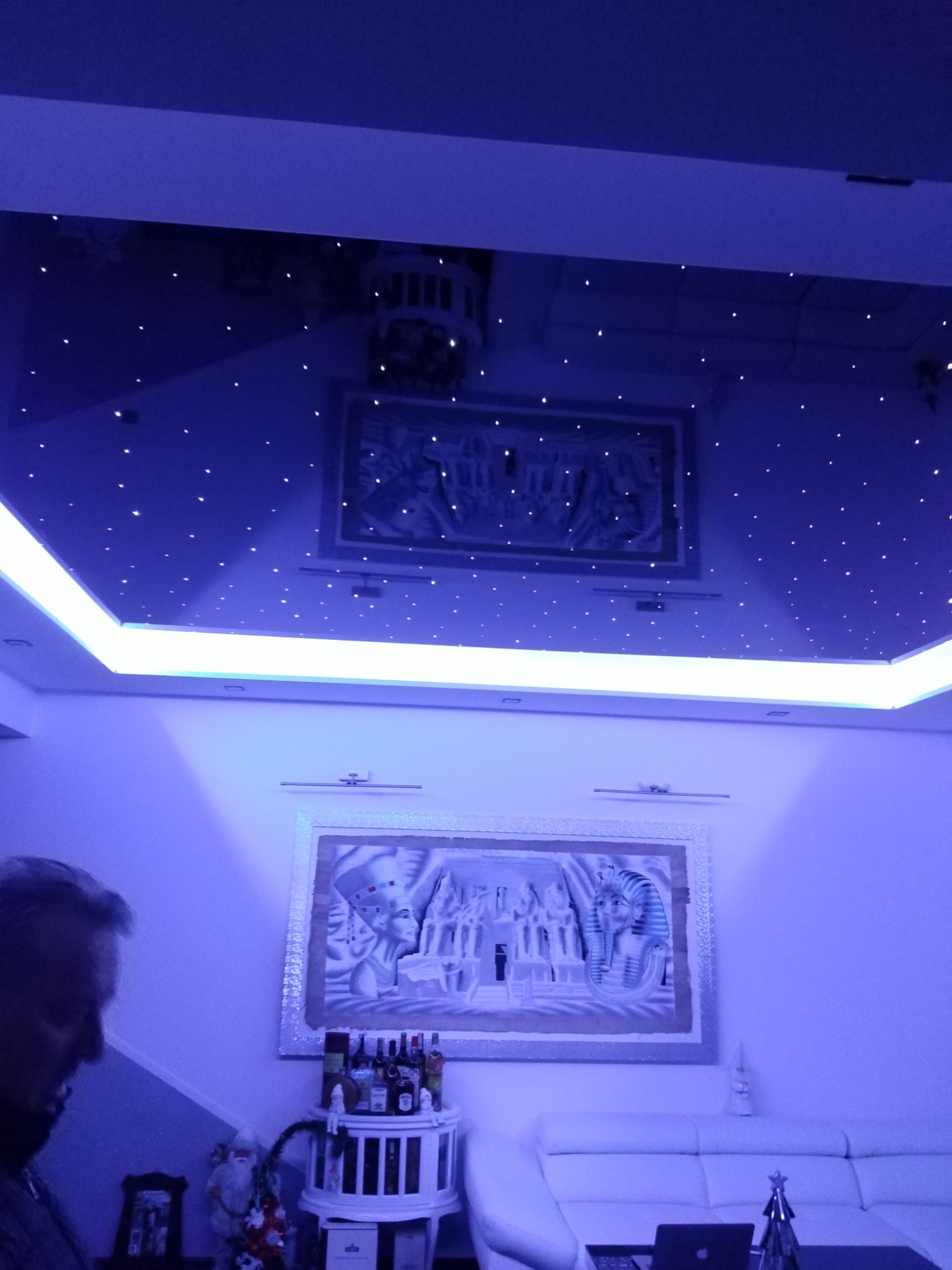 Salon z sufitem podwieszanym imitującym nocne niebo, oświetlonym punktowymi diodami LED i listwą LED, dodatkowo dekoracje na ścianach w stylu egipskim.