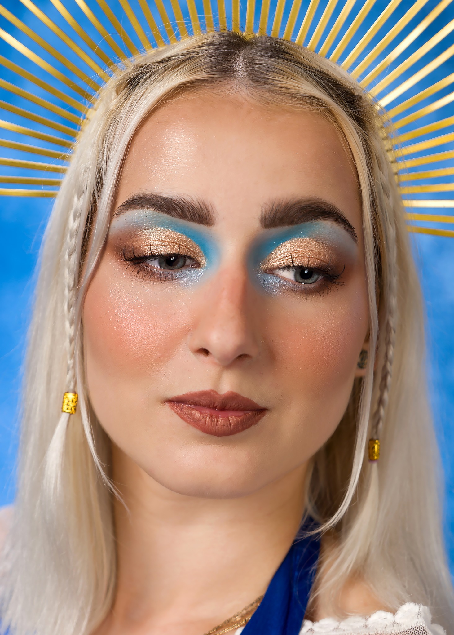 Portret kobiety z platynowymi włosami, złotą aureolą i intensywnym makijażem oczu w odcieniach błękitu i złota, wykonany w studio fotograficznym w Wieliczce.