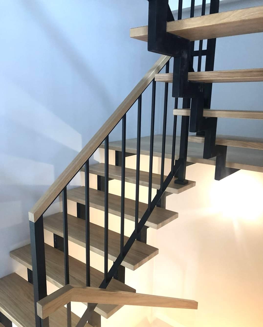 Nowoczesne schody z drewnianymi stopniami i czarnymi metalowymi wspornikami oraz jasną drewnianą poręczą, widok od dołu.