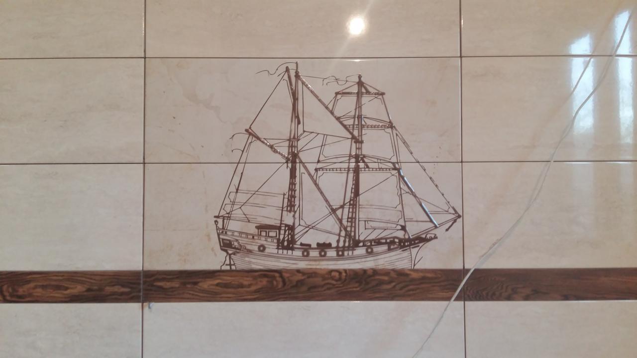 Ściana z beżowych płytek ceramicznych z brązowym akcentem i rysunkiem żaglowca w stylu szkicu.