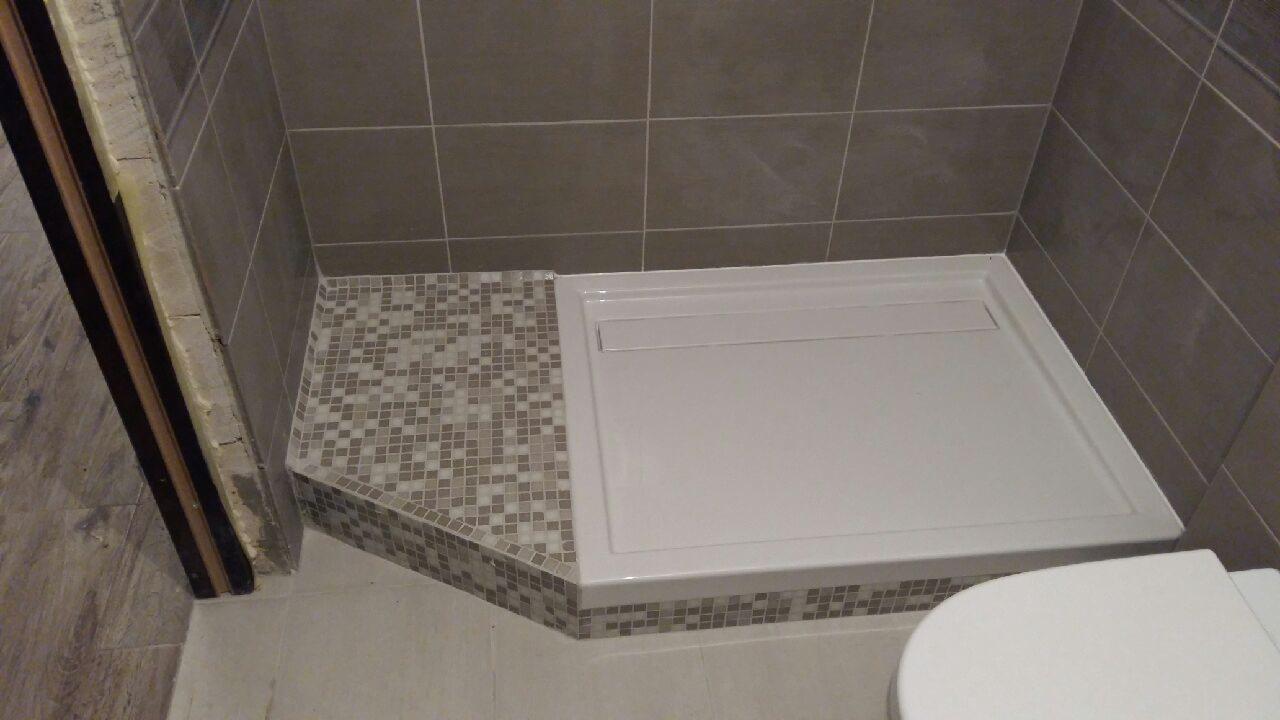 Nowoczesna kabina prysznicowa z brodzikiem, wykończona mozaiką w odcieniach szarości, z widocznymi szarymi płytkami na ścianach i fragmentem toalety w prawym dolnym rogu.