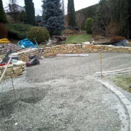 Przygotowany teren pod budowę okrągłego tarasu z kamienia, widoczny ubijak, poziomica i narzędzia, w tle ogród.