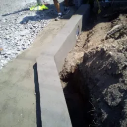 Betonowy obrzeże chodnika w trakcie budowy, widoczny wykop i przygotowane podłoże z kruszywa.