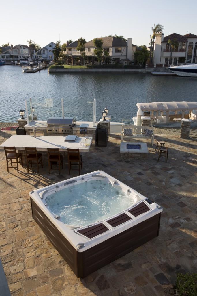 Luksusowy taras nad wodą z jacuzzi, grillem, barem i miejscem do siedzenia, widok na rezydencje i zacumowane łodzie.