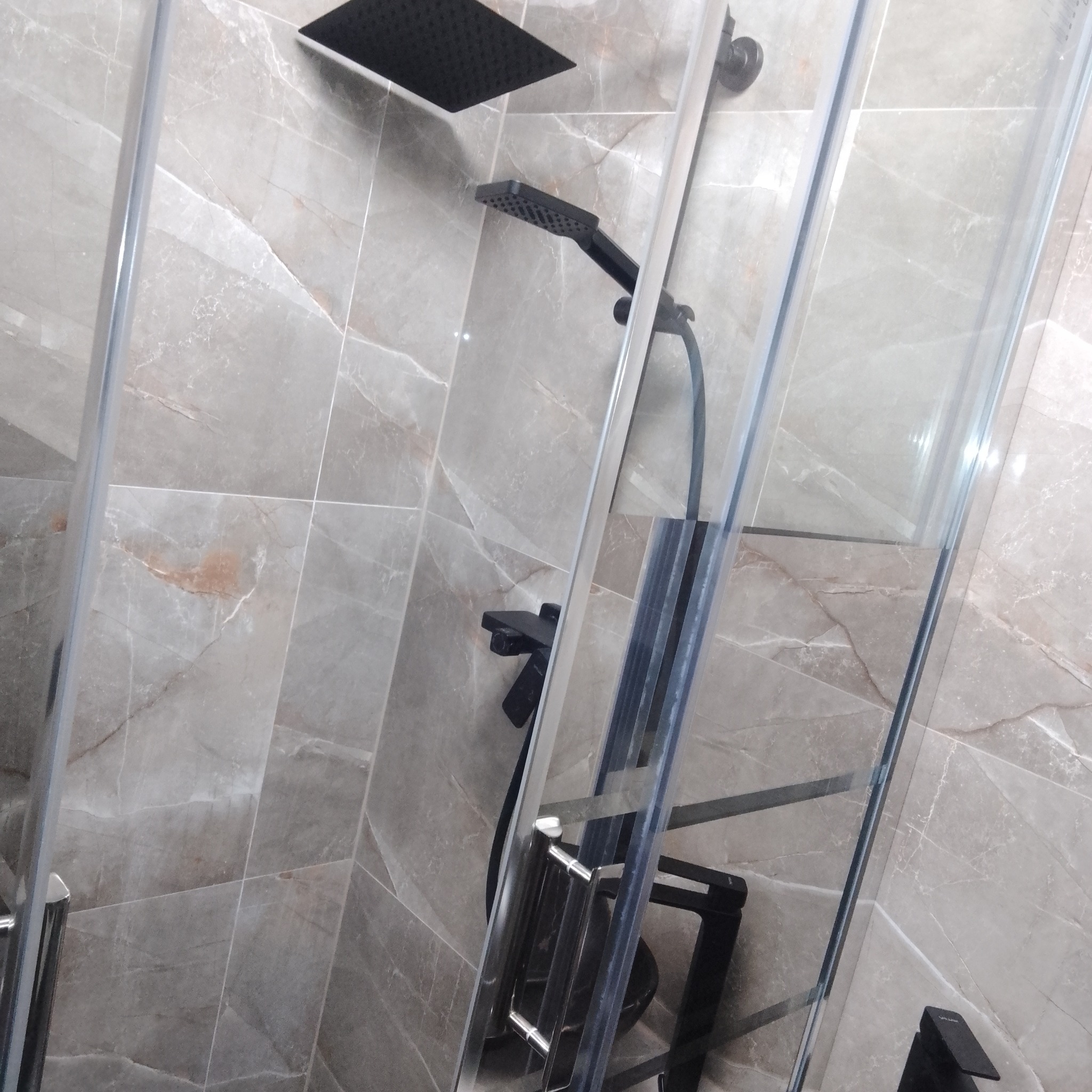 Nowoczesna kabina prysznicowa z czarną armaturą na tle szarych płytek imitujących marmur.