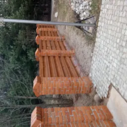 Nowo wybudowany, drewniano-ceglany płot oddzielający posesję od lasu, widoczny kosz do koszykówki i fragment chodnika z kostki.