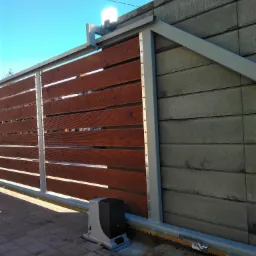 Automatyczna brama przesuwna z drewnianymi panelami, szarą ramą i napędem elektrycznym na tle betonowego muru.