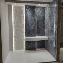 Wnętrze łazienki w trakcie remontu, z fragmentami ścian pokrytymi płytkami imitującymi marmur, ścianą z trójwymiarową białą mozaiką i białymi płytkami podłogowymi, oświetlenie punktowe w suficie...