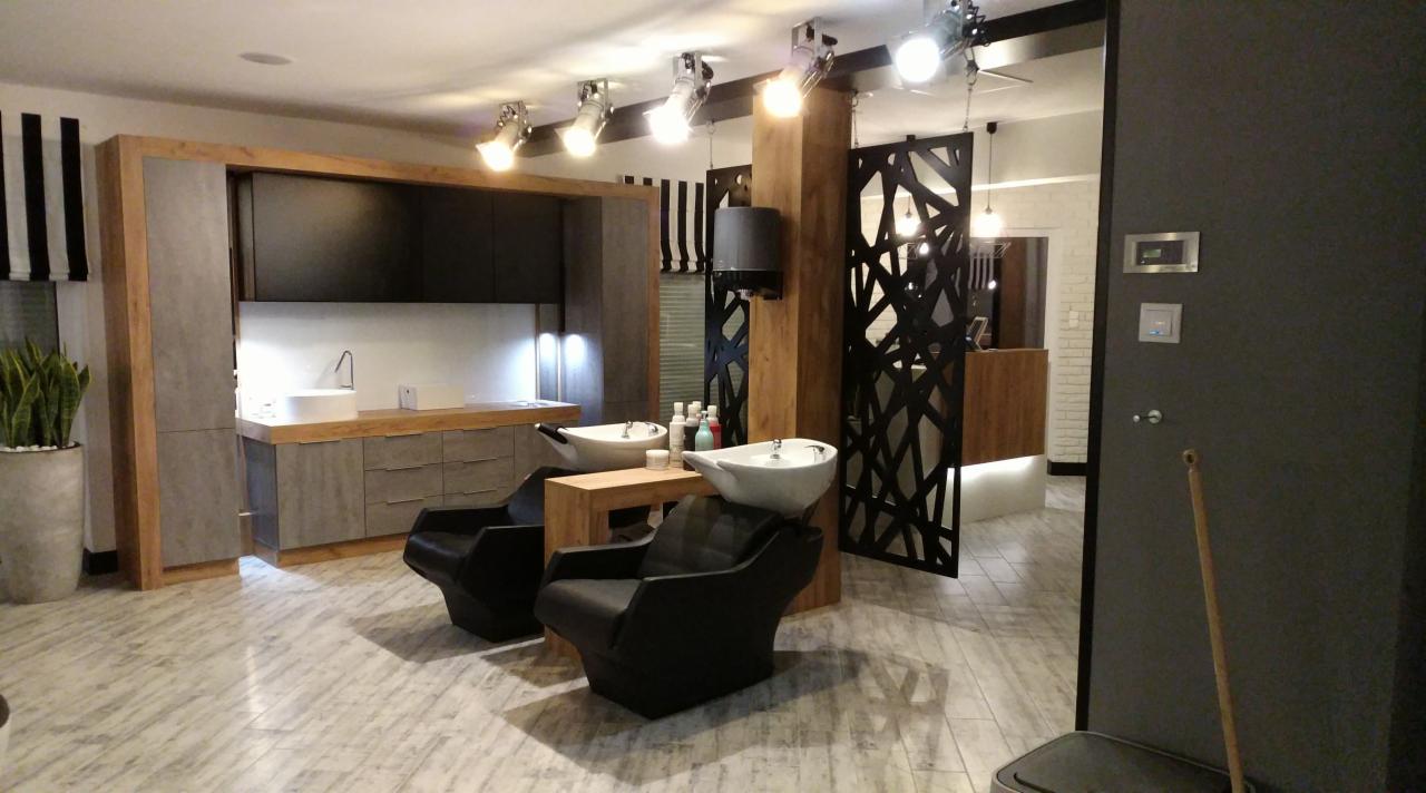 Nowoczesne wnętrze salonu kosmetycznego z dwoma stanowiskami do zabiegów na dłonie i stopy, wyposażonymi w białe umywalki i czarne, skórzane fotele. W tle widoczna zabudowa meblowa z szarymi...