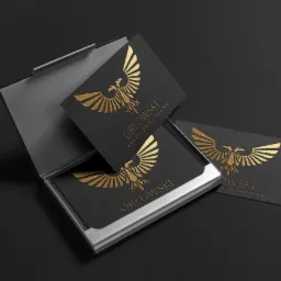 Wizytówki z tłoczonym złotym logo orła i nazwą kancelarii prawnej w metalowym etui na ciemnym tle.