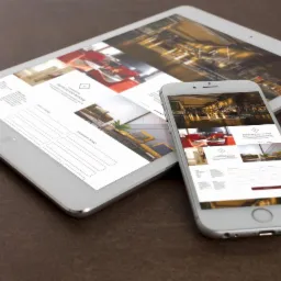 Tablet i smartfon wyświetlające ten sam projekt strony internetowej, z widocznymi elementami interfejsu i formularzami kontaktowymi, leżące na brązowym tle.