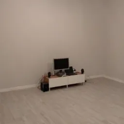 Pusty pokój z ułożonymi panelami podłogowymi w odcieniach szarości, białe listwy przypodłogowe, ściany pomalowane na szaro, widoczne gniazdka elektryczne bez osprzętu i meble RTV z podłączonym...