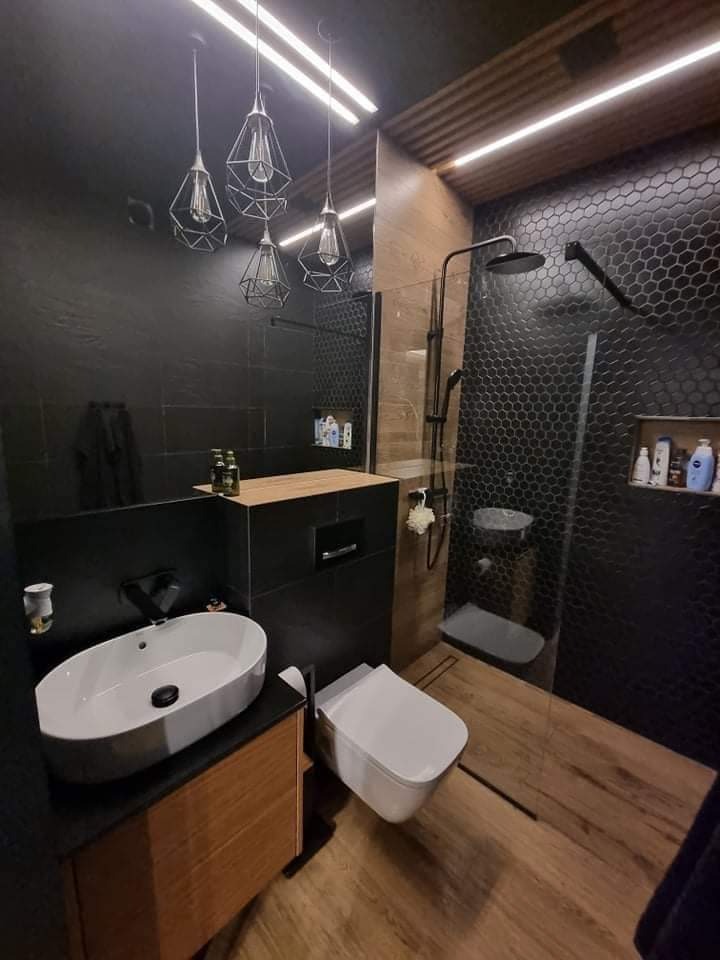 Nowoczesna łazienka z czarnymi płytkami heksagonalnymi pod prysznicem, drewnianą podłogą i wiszącymi lampami w stylu industrialnym.