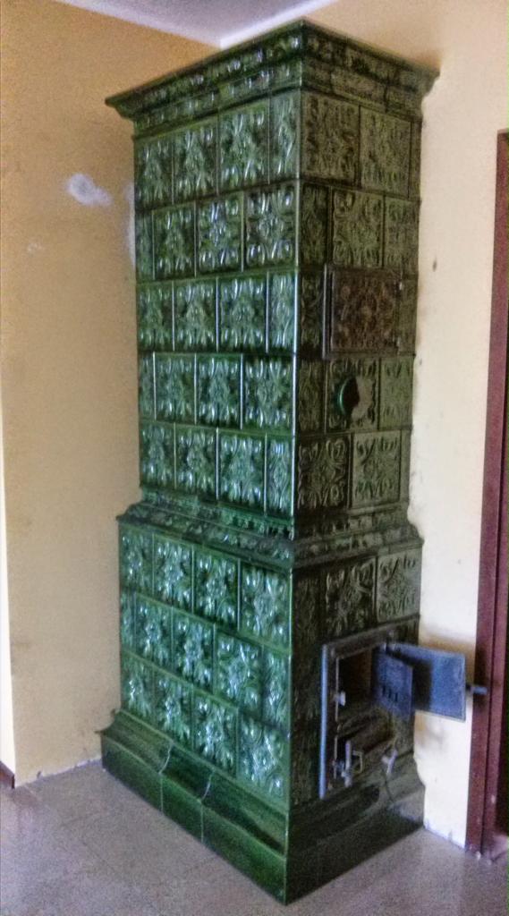 Zielony, kaflowy piec zdobiony wzorami, z otwartymi drzwiczkami paleniska, zrealizowany w Gdyni.