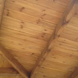 Drewniany strop z widocznymi belkami nośnymi, wykonany z jasnego drewna z wyraźnym usłojeniem, ujęcie z dołu pod kątem.