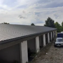 Nowy, ciemnoszary dach z blachy na budynku garażowym z białymi kolumnami, widok z zewnątrz, samochód osobowy zaparkowany obok.